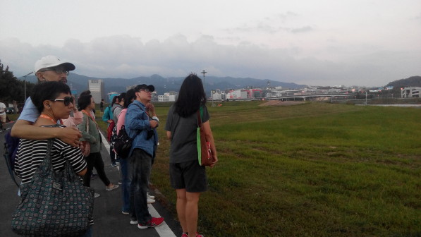 參與活動的眾人在基隆河岸草坪前駐足